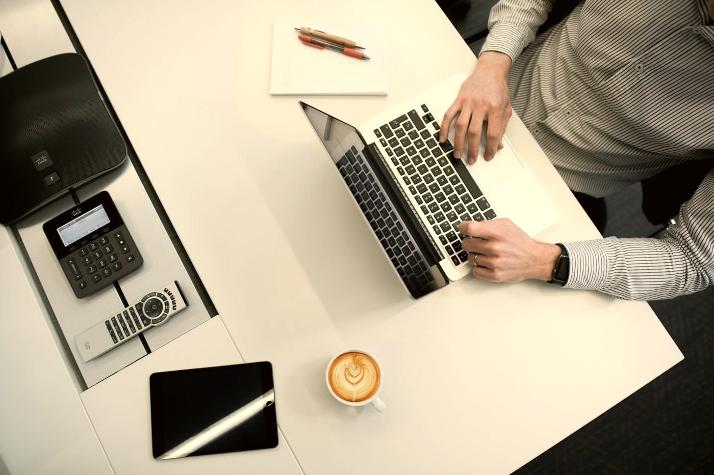 A laptop, phone and coffee on a white desk from above